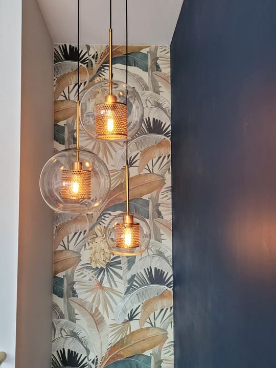 Three blown-glass pendants hung over a papered feature wall — the warm end of a lighting job.