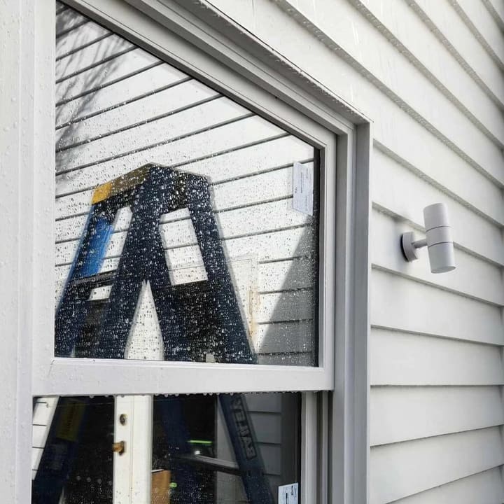 Ladder up at the window to run a new exterior light on weatherboard cladding.